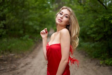 Beautiful Young Long Haired Blonde In A Red Dress Posing On The Road In A Summer Park With A