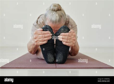 Senior Active Female Holding Her Feet While Bending Forwards And