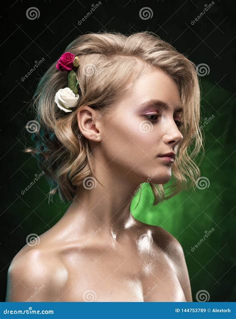 Het Mooie Jonge Blondemeisje Met Naakte Die Schouders Bloemen In Haar Haar En Olieachtig