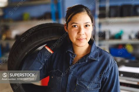 Mixed Race Female Car Mechanic Wearing Overalls Holding Tire Looking