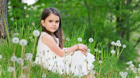 Cute Little Girl Is Sitting On Green Grass Surrounded By White