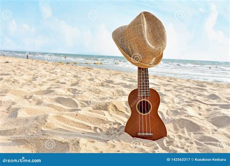 Acoustic Ukulele Standing in the Sandy Beach with Hat Stock Image