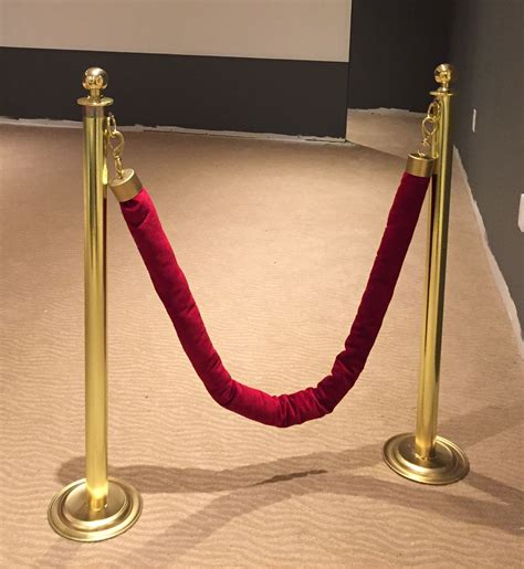 A Roped Off Red Carpeted Area With Two Gold Posts And A White Screen In