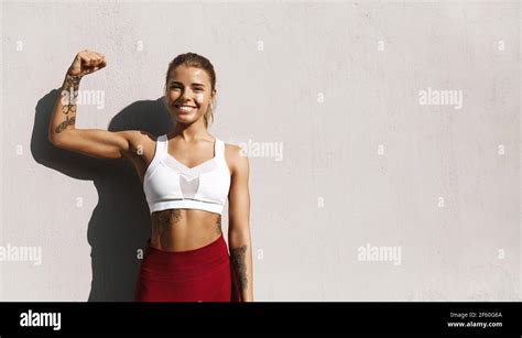 Outdoor Shot Of Young Female Athlete Flexing Muscles Showing Strong Arm Biceps And Smiling