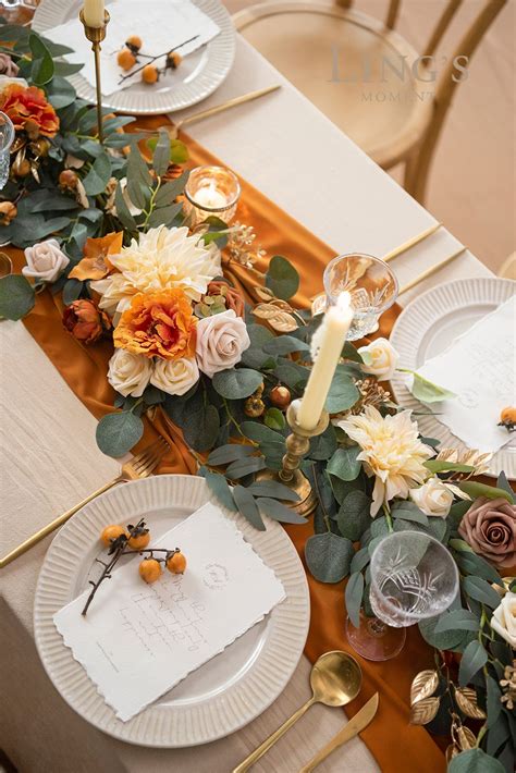 The Table Is Set With White Plates And Gold Place Settings Orange Napkins And Flowers