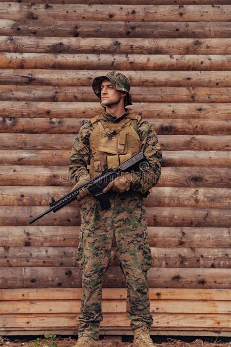 A Soldier In Uniform With A Rifle In His Hand Is Standing In Front Of A