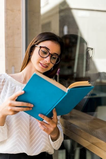 Free Photo Young Lady With Glasses Reading Book Leaning On Window