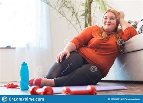 Chubby Woman Sport At Home Sitting On Mat Leaning On Sofa Relaxed