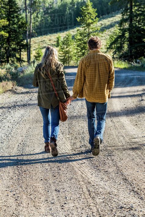 Caucasian Couple Walking On Dirt Road Holding Hands Stock Photo