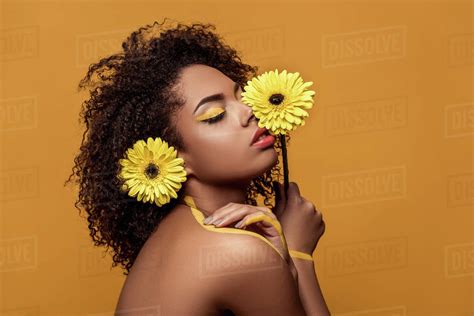 Stylish African American Woman With Artistic Make Up Holds Flower By Her Face Tenderly Touches
