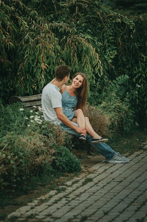 Прекрасная влюбленная пара сидит в парке на скамейке летом обнимается