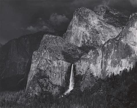 An Old Black And White Photo Of A Waterfall In Front Of Some Mountains With Clouds
