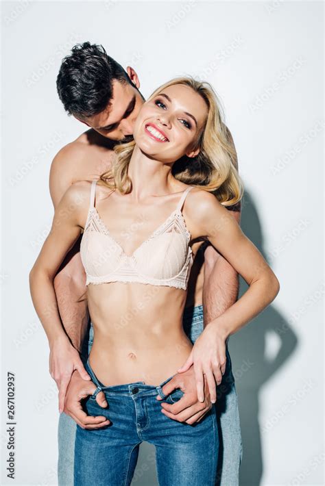 Handsome Man Kissing Cheerful Blonde Girl In Lace Bra Standing In Jeans On White Stock Photo