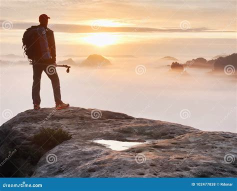 Tired Hiker With Sporty Backpack On Rocky Peak And Watching Into Deep Misty Valley Bellow Stock