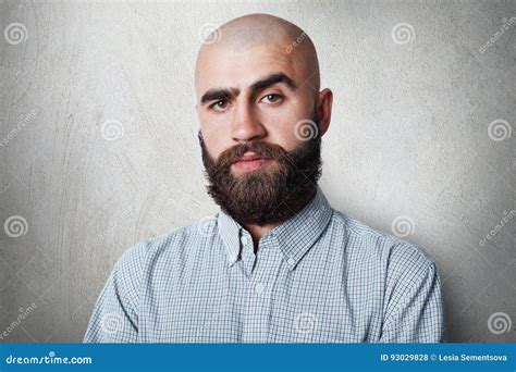 A Confident Bald Male With Thick Black Eyebrows And Beard Wearing