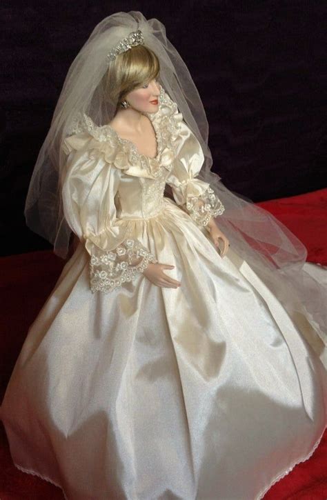 A Doll Dressed In A Wedding Dress And Veil On A Red Cloth Covered Tablecloth