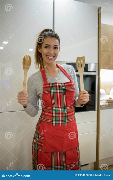 Beautiful Young Woman Standing In A Kitchen Wearing An Apron While