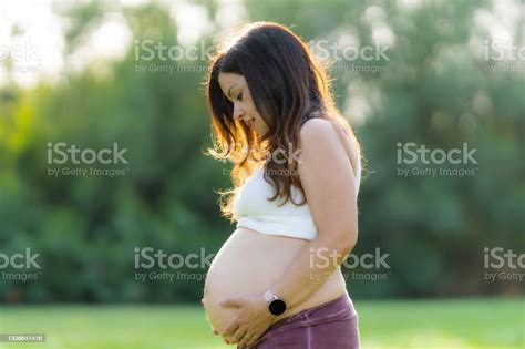 Pregnant Woman Touching Her Abdomen In A Park With The Sunlight Shining