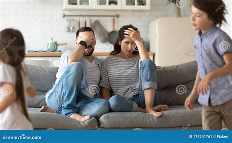 Tired Young Parents Exhausted From Loud Kids Playing Stock Image