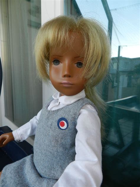 a doll with blonde hair sitting in front of a window