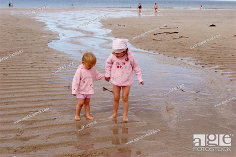 4 And 2 Year Old Girls Standing On The Beach Holding Hands Laughing