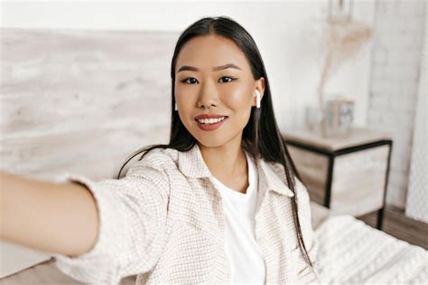 Atractiva Mujer Asiática Con Chaqueta A Cuadros Beige Y Camiseta Blanca Sonríe Y Se Toma Selfie