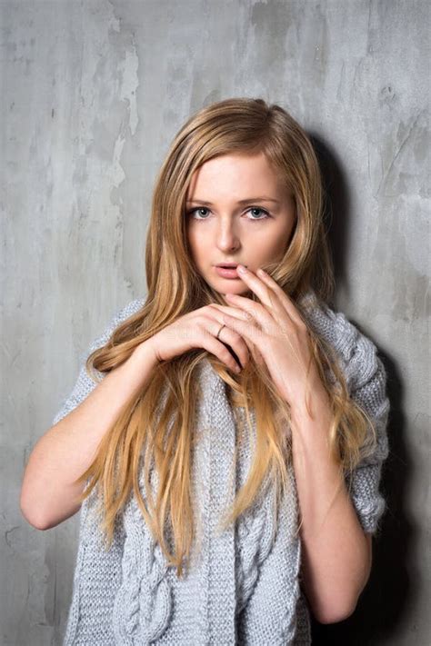 Young Longhair Blonde Woman In Knitted Sweater Posing Against Grungy Gray Wall Scared Or