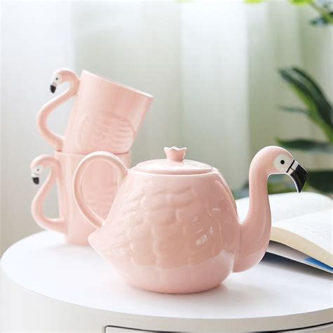 Two Pink Flamingo Teapots Sitting Next To An Open Book
