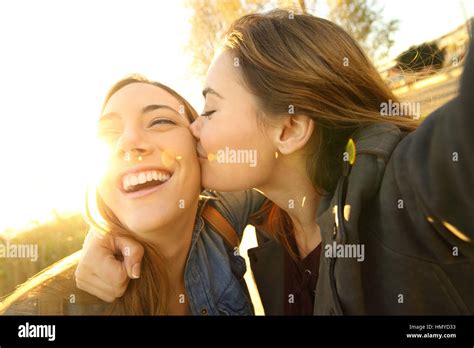Two Affectionate Friends Kissing And Taking A Selfie Outdoors In The
