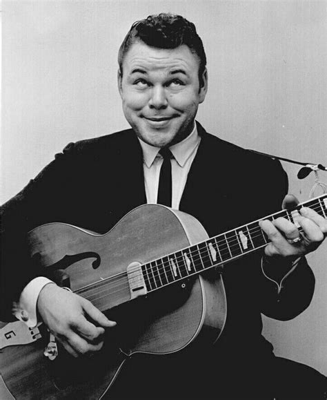 A Black And White Photo Of A Man Holding An Acoustic Guitar In His