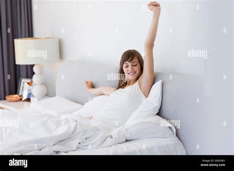 Happy Woman Waking Up And Yawning With A Stretch While Sitting In Bed