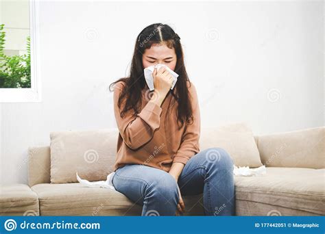 An Asian Woman Has A Headache And A Runny Nose Sitting On The Sofa In