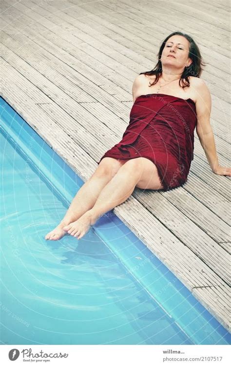 Mature Brunette Woman Sunbathing By The Pool With Her Feet In The Water Wrapped In A Bath Towel