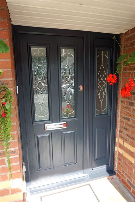 A Black Front Door With Two Glass Panels And Red Flowers On The Side