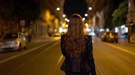 Tourist Woman Walk Away From The Camera At Night While Walking The City