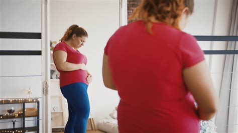 Young Overweight Woman Feeling Sad Because Of Excess Weight Looking At Herself At Mirror Stock