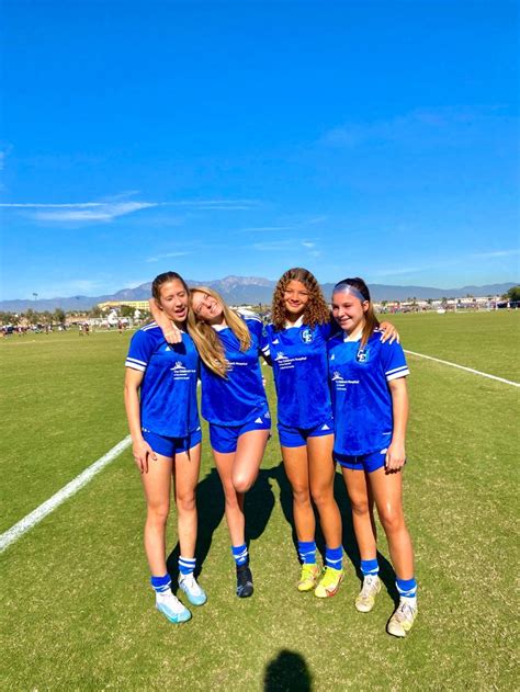 Four Girls In Blue Uniforms Standing On A Soccer Field With Their Arms