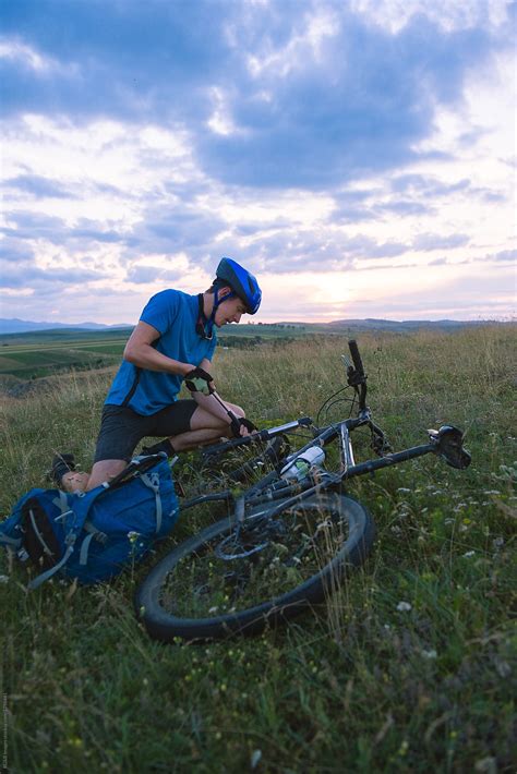 Man Fixing His Mountain Bike On Green Meadow During Sunset Del Colaborador De Stocksy Ibex