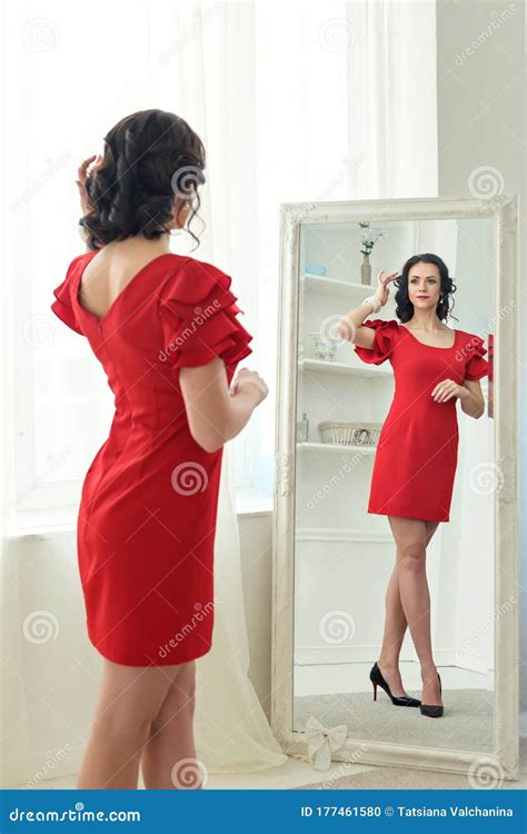 Young Brunette Woman Stands Looking In Reflection In A Full Length
