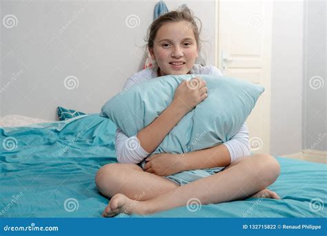 A Pensive Teenager Girl With Pillow Sitting Cross Legs On Bed Stock