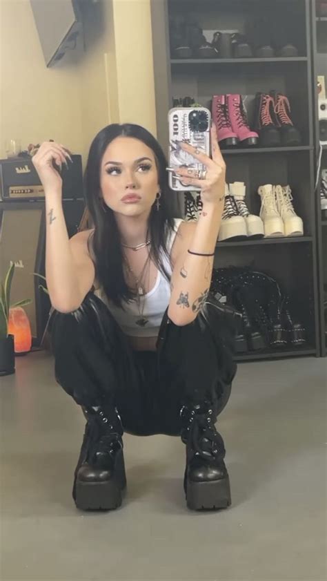 a woman kneeling on the ground taking a selfie with her cell phone while wearing black boots