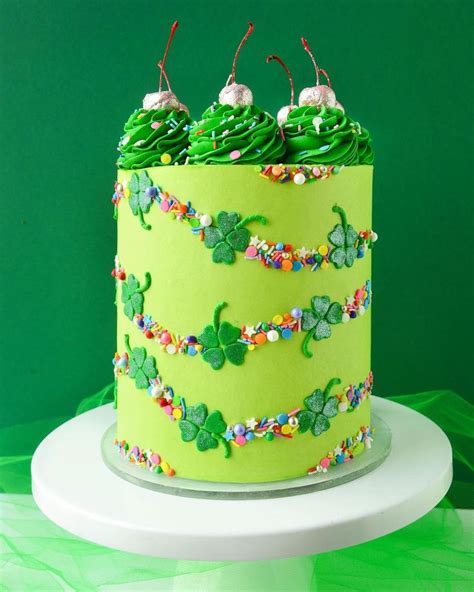 A Green Cake Decorated With Shamrocks And Candies On A White Pedestal Against A Green Background