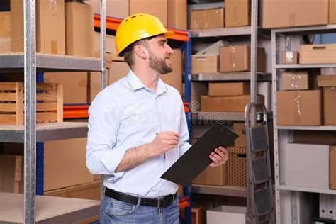 Young Man With Clipboard Near Rack Of Boxes At Warehouse Stock Photo