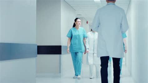 Female Surgeon And Female Doctor Walk Through Hospital Hallway Talking