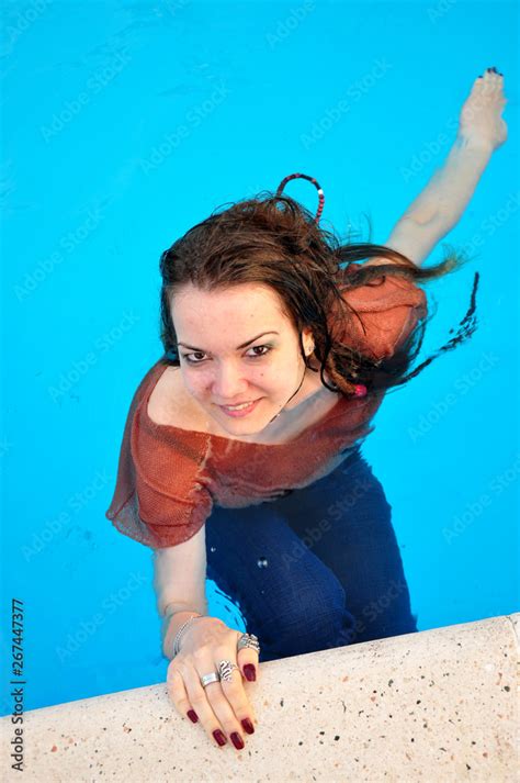fully dressed girl swimming in the pool wearing her wet clothes on on a hot summer day stock