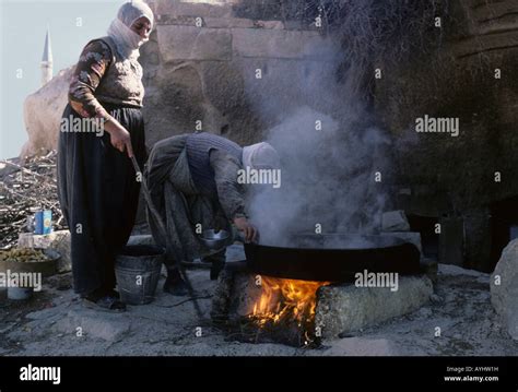 two turkish women cook food over an open fire beneath the walls and minaret of a mosque in