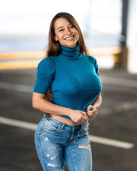 A Woman In Blue Shirt And Jeans Posing For The Camera With Her Hands On