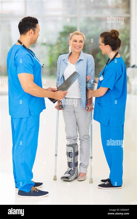 Friendly Healthcare Workers With Injured Woman On Crutches In Hospital