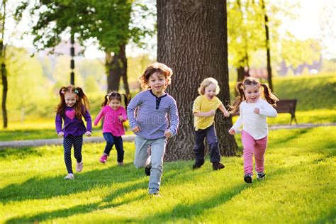 Many Young Children Smiling Running Along The Grass In The Park Stock
