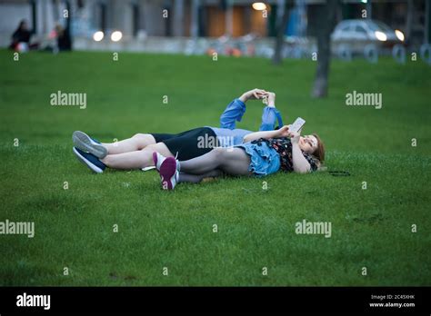 Two Young People Lie Down On The Lawn Staring At Their Mobile Phones